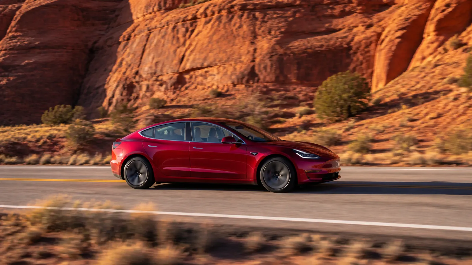 Red Tesla Model 3 driving through a Utah red-rock canyon